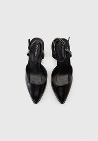 Mustat nahkaiset slingback-korkokengät teräväkärkisellä muotoilulla ja sileällä pinnalla. Omistaa ohuen nilkkastrapin, jossa on pieni solki. Brändilogo näkyvissä sisäpuolella.