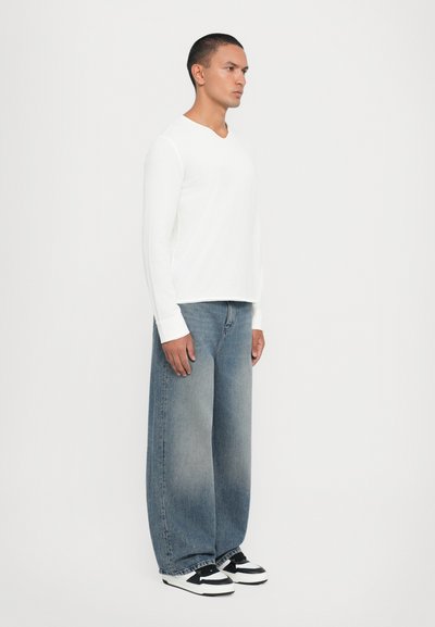 Chemise blanche à manches longues avec un col en V, associée à un jean en denim bleu clair surdimensionné et des baskets noir et blanc.