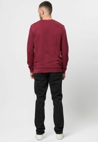 Burgundska dolgi rokav sweatshirt s okroglim ovratnikom, prilegajočimi manšetami in ravnim robom, v kombinaciji z črnimi hlačami in belimi teniskami.