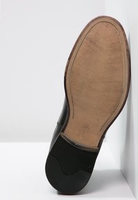 Czarny skórzany elegancki but o gładkim wykończeniu; kontrastowa podeszwa o fakturze przypominającej drewno z gumowymi akcentami; szczegółowe przeszycia wzdłuż krawędzi.