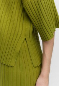 Ribbed knit dress in bright green. Features wide sleeves, vertical lines, and side slits. Soft texture with a streamlined silhouette.