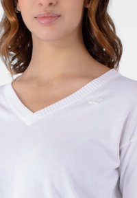 Maglione bianco a scollo a V realizzato in morbido tessuto con collo a coste, caratterizzato da un piccolo simbolo decorativo sul lato sinistro e una superficie liscia.