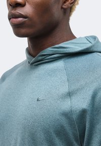 Κοντινό πλάνο ενός ατόμου που φοράει ένα ανοιχτό μπλε φούτερ με κουκούλα και μικρό λογότυπο Nike στο στήθος.