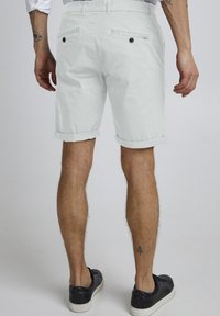 Pantalones cortos blancos con puños enrollados, hechos de un tejido ligero, que cuentan con dos bolsillos traseros con botones y una textura sutil en la superficie.