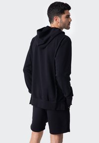 Czarna bluza z kapturem, z kieszenią kangurzą i sznurkiem do regulacji, w zestawie z dopasowanymi szortami. Materiał wydaje się miękki o gładkiej fakturze.
