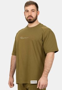 T-shirt oversize vert olive en tissu doux, avec un col rond, des manches courtes et un détail d'étiquette à l'ourlet avec un logo brodé.