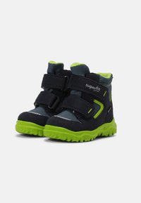 Stivaletti per bambini con tomaia in tessuto blu scuro, suola in gomma verde e doppie cinghie in Velcro. Presentano una morbida fodera interna e dettagli riflettenti.