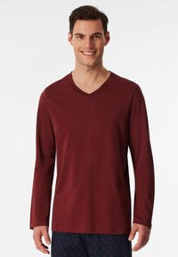 Maglietta a maniche lunghe color marsala con scollatura a V realizzata in tessuto morbido, caratterizzata da una vestibilità rilassata e dettagli di cucitura minimi. Adatta per un abbigliamento casual.