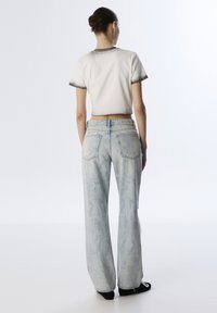 Korte witte t-shirt met grijze accenten, gecombineerd met lichtblauwe, wijdvallende, distressed jeans. Soepele stof, relaxte pasvorm en subtiel patroon.