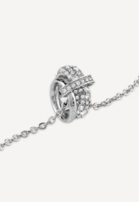 Gioiello in tonalità argento con un charm rotondo e testurizzato, incastonato di cristalli trasparenti e una catena collegata per il fissaggio.