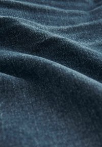 Donkerblauwe denimstof met een gestructureerd oppervlak, met zachte, gevouwen golven die een subtiele glans en diepte creëren.