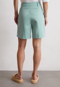 Mintgrüne Stoffshorts mit glatter Textur, ausgestattet mit einer Gesäßtasche und kombiniert mit beigen, gewebten Keilsandalen.