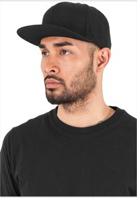 Casquette de baseball noire à visière plate, en tissu. Portée avec un t-shirt noir à col rond, mettant l'accent sur des couleurs simples et solides ainsi qu'un design épuré.