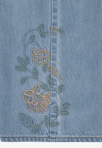 Svetle modrá džínová tkanina s květinovou výšivkou v růžové a žluté barvě, se zelenými listy. Podrobný steh podél vertikálního švu.