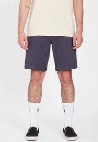 Donkere marineblauwe korte broek gemaakt van zachte stof, met een comfortabele pasvorm en een rechte zoom. Gecombineerd met een lichtgekleurde T-shirt en zwarte instapschoenen.