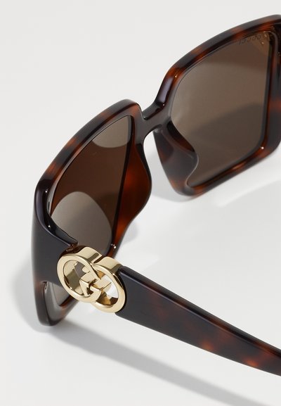 Γυαλιά ηλίου καβουροειδούς με καφέ φακούς, που διαθέτουν τολμηρούς, γωνιώδεις σκελετούς και έναν χρυσό διπλό λογότυπο G ως διακόσμηση στους βραχίονες.