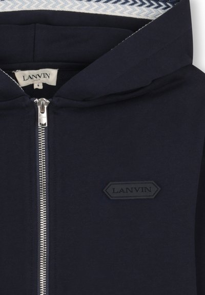 Sweat à capuche zippé bleu marine avec une fermeture éclair argentée, une doublure intérieure texturée de la capuche, et un patch logo LANVIN noir sur le côté gauche de la poitrine.