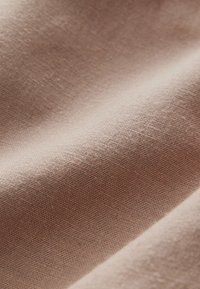 Weicher, beiger Stoff mit feiner, strukturierter Webart, der einen subtilen Glanz und einen sanften Fall zeigt. Hervorhebung einer gleichmäßigen, konsistenten Oberfläche.