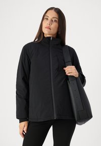 Black insulated jacket with a high collar and front zipper, featuring a chest pocket and smooth texture, paired with a matte black shoulder bag.