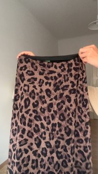 Leoparda raksta svārki ar brūnu pamatni un tumši brūniem plankumiem, izgatavoti no mīksta auduma, ar melnu jostasvietu un vieglu spīdumu.