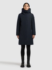 Marineblauwe parka met een hoge kraag en grote capuchon, voorzien van ritssluitingen aan de zijkanten, een strak ontwerp en een midilange snit. Zwarte enkellaarzen worden getoond.