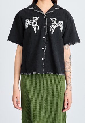 Czarna koszula z krótkim rękawem, z białymi haftowanymi motywami jeleni, kontrastowym przeszyciem i zapięciem na guziki. Teksturowana tkanina i luźny krój.