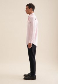Camisetta rosa chiaro a maniche lunghe, slim fit, con polsini con bottone, abbinata a pantaloni scuri e scarpe nere; design minimale e texture liscia.
