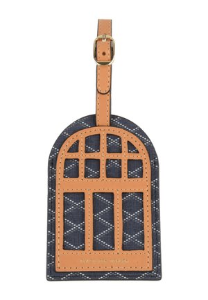 Étiquette de bagage avec cadre et sangle en cuir fauve sur tissu bleu marine orné de points blancs diagonaux. Texte « PLACE DES VOSGES » embossé près du bas.