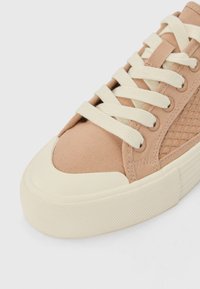 Sneaker beige in tela con pannello laterale in rete testurizzata, suola in gomma crema e lacci bianchi. Punta arrotondata e cuciture rinforzate visibili.