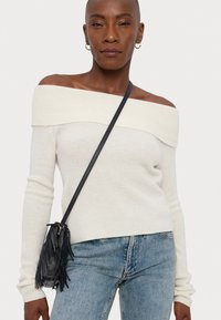 Off-white rebrasto pulover z odprtimi rameni in dolgimi rokavi; kombiniran z modrimi trapercami in majhno črno torbico s frufruji.