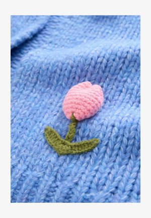 Kék kötött anyag texturált mintával, amelyen egy rózsaszín horgolt tulipán és zöld szár található, dekoratív elemet kölcsönözve.