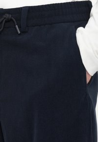 Námorníctvo modré kordové tepláky s elastickým pásom a šnúrkou. Obsahuje bočné vrecká a textúrovanú tkaninu. Detailný záber zvýrazňuje materiál.