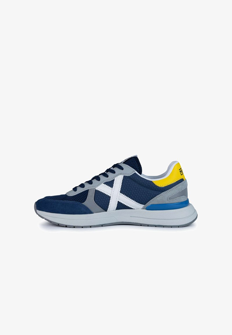 Zapatillas azul y gris con materiales de malla y gamuza, que presentan franjas de acento blancas, una pestaña en el talón amarilla y una suela texturizada.