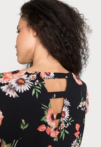 Vestido preto floral com um padrão vibrante de flores brancas e cor-de-rosa, com detalhe nas costas em recorte e alças. Textura suave.