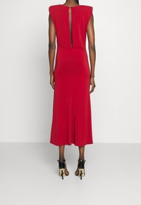 Robe midi rouge avec des manches courtes, détail de trou de serrure dans le dos et silhouette ajustée. Tissu léger et lisse avec un léger brillant.
