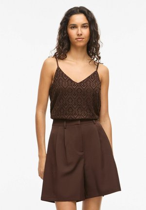 Femme portant un haut marron sans manches texturé avec un motif en losange et un short marron taille haute à jambes larges, debout sur fond blanc.