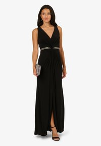 Černé bezramínkové šaty s hlubokým V-výstřihem, vypasovaným korzetem, zkrouceným detailem a třpytivým páskem. Dlouhá, splývavá látka s bočním rozparkem.