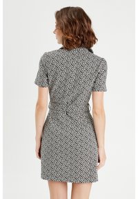 Robe à manches courtes, noire et blanche avec un motif, dotée d'une taille cintrée, d'un col et d'un détail de nœud au dos. Tissu lisse avec un design géométrique.
