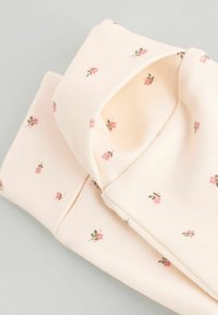 Ljusrosa tyg med små blommönster i mörkare rosa och grönt, vikt med synlig textur och sömdetaljer.
