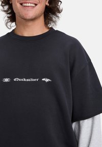 T-shirt nera oversize con maniche corte, caratterizzata da un logo "Quiksilver" bianco e grafiche sul davanti. Tessuto morbido.