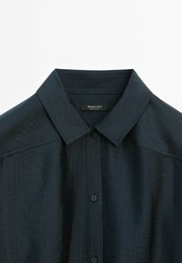 Chemise bleu marine foncé à boutons avec col pointu et tissu subtilement texturé, affichant l’étiquette Massimo Dutti à l’intérieur du col.