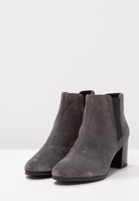 Botas de tobillo de ante gris con punta afilada y tacón medio cuadrado. Presentan paneles laterales elásticos para un fácil uso y una textura suave.
