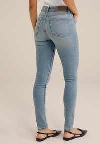 Ljusblå skinny jeans i denim, med hög midja, bakfickor och subtila blekningar. Tillbehör med svarta platta skor.