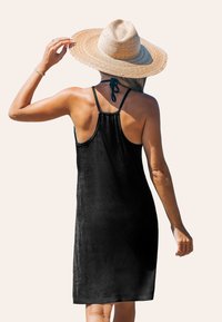 Vestido negro sin mangas con un corte relajado, hecho de una tela suave, con tirantes finos y la espalda fruncida, acompañado de un sombrero de paja.