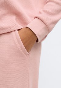Svetloružová textúrovaná látka s voľným strihom a bočným vreckom. Rukávy s manžetami poskytujú pevné zakončenie.