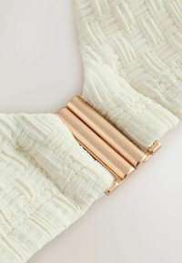 Close-up of textured white fabric connected by a smooth, shiny rose gold metal clasp.