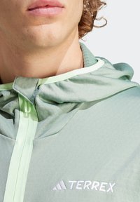 Chaqueta con capucha TERREX de color verde claro, con una textura suave, cierre frontal y ribetes en un verde claro en contraste. Presenta un logotipo bordado en el pecho.