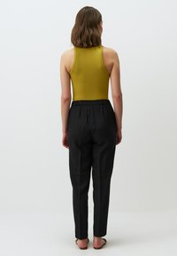 Olivengroene geribbelde bodysuit met een hoge halslijn, gecombineerd met zwarte, losse broek met een elastische tailleband.