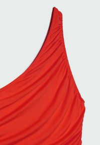 Haut de maillot de bain rouge vif avec une texture plissée et froncée, à bretelle unique, sur un fond clair.