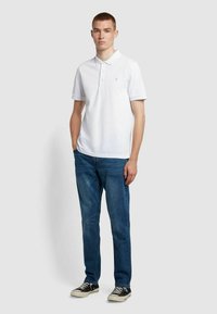 Witte polo met korte mouwen, drieknoopsluiting en klein logo. Gekozen in combinatie met blauwe jeans en zwarte sneakers. Casual pasvorm.